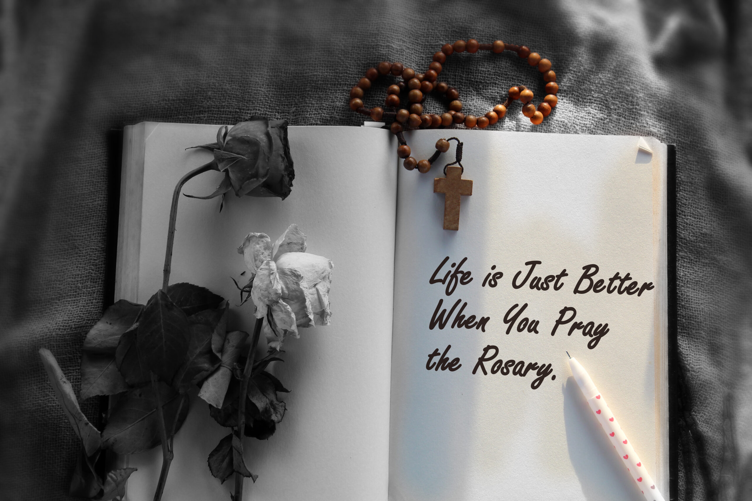 Inspirational motivational quote - Life is just better when you pray the Rosary. With Wooden Rosary beads and Jesus Christ holy cross crucifix, dried wilted roses on the open book on the table.